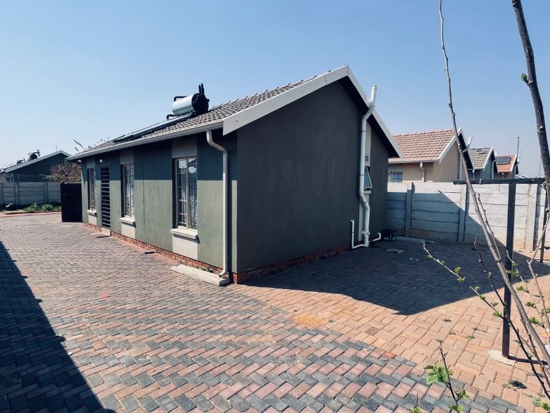 Rear view of the property featuring a paved yard, precast boundary wall, and a roof-mounted solar water heating system.