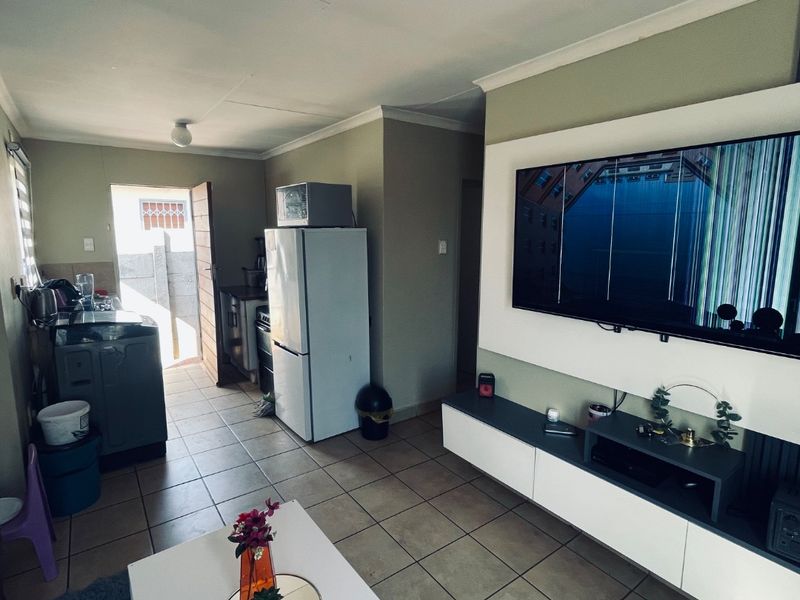 Open-plan living area featuring tiled flooring, a built-in media console, and an adjacent kitchen space with direct access to the exterior.