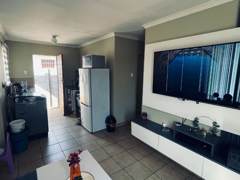 Open plan living area featuring tiled flooring, a built-in media console, and an adjacent kitchen space with direct access to the exterior.