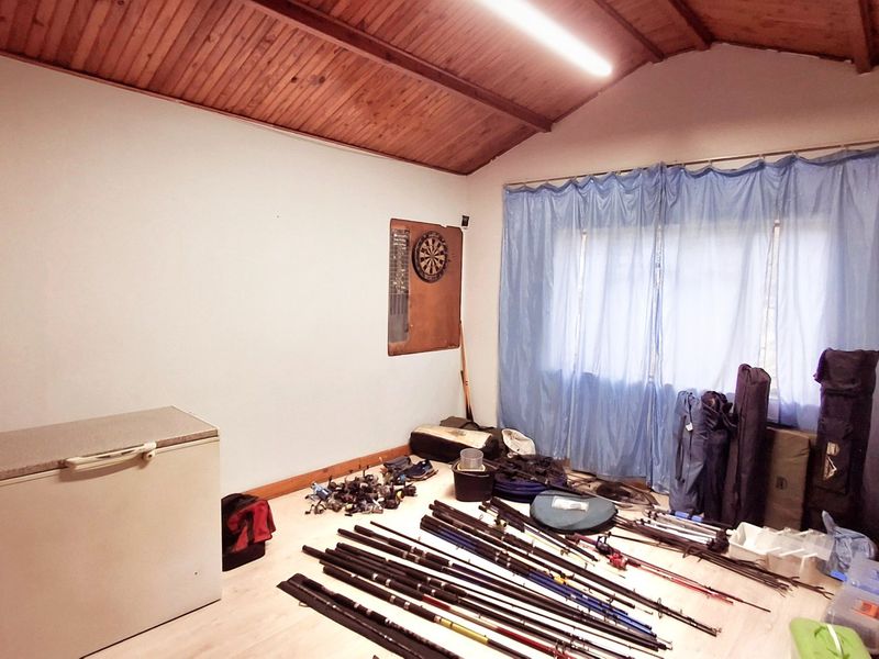 A utility space featuring an exposed timber vaulted ceiling, laminate flooring, and fluorescent lighting, currently utilized for storage.