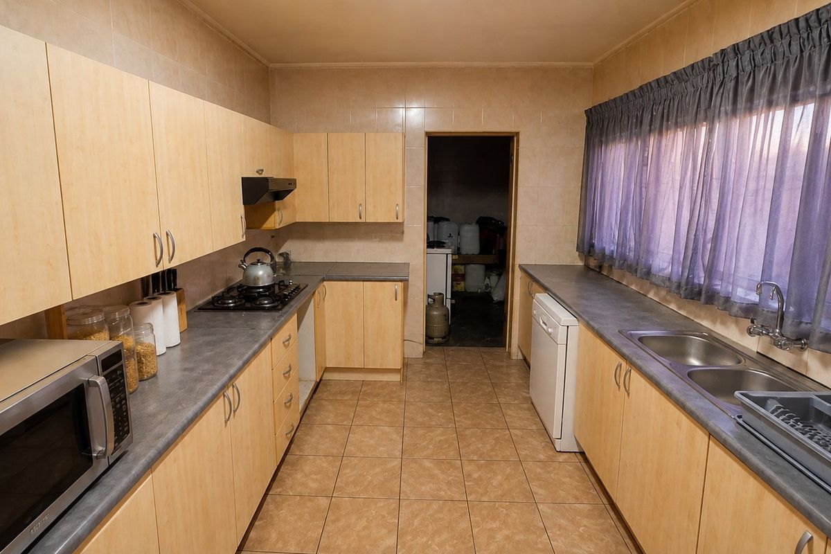 Functional kitchen featuring light wood-finish cabinetry, laminate countertops, a gas hob with extractor, and tiled finishes throughout.