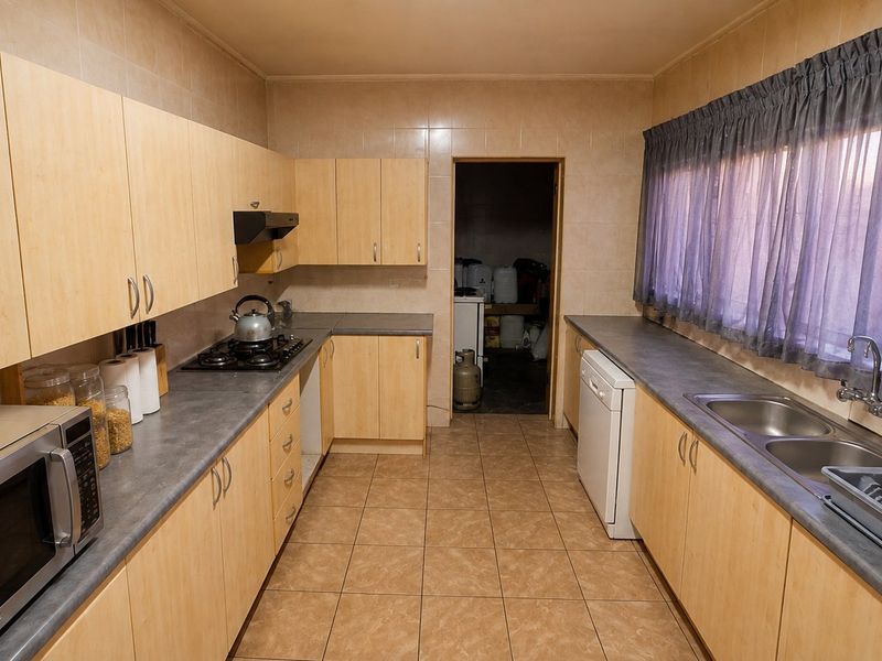 Functional kitchen featuring light wood-finish cabinetry, laminate countertops, a gas hob with extractor, and tiled finishes throughout.