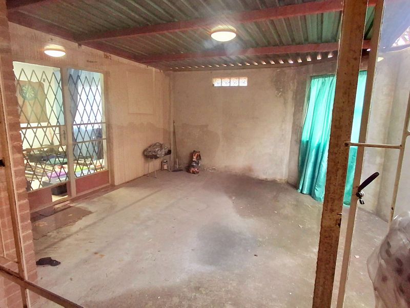 A covered outdoor patio area featuring a concrete floor, corrugated metal roof, and security gate access to the main living space.