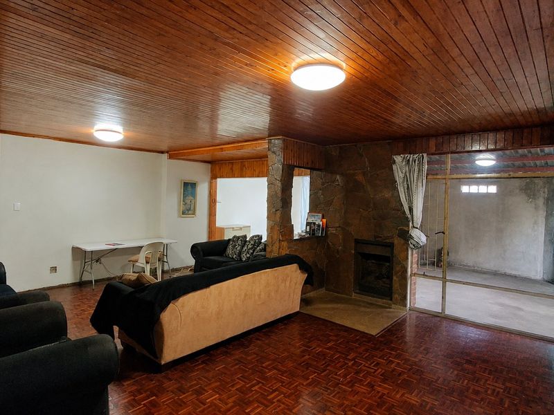 Spacious living room featuring a stone fireplace, timber-clad ceiling, and parquet flooring, with direct access to an adjacent enclosed patio area.
