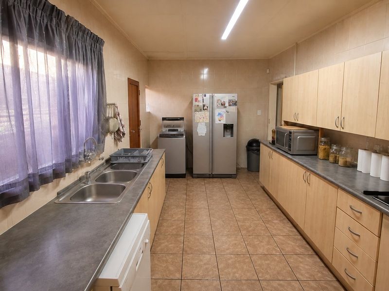 A functional galley-style kitchen featuring light wood-finish cabinetry, dark countertops, tiled walls, and a gas hob with an integrated extractor fan.