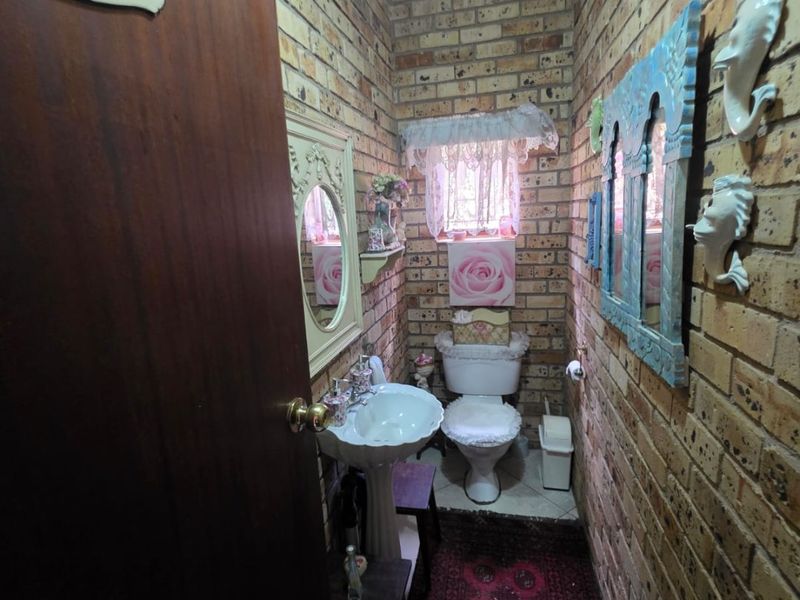 A compact bathroom featuring exposed brick walls, a pedestal basin, and a toilet, offering a rustic aesthetic with potential for modernization.