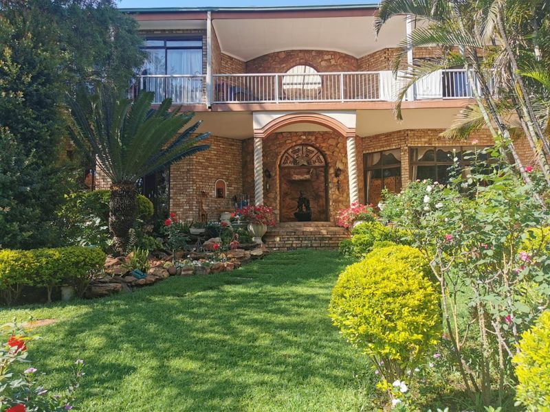 A charming two-story brick residence featuring stone cladding, an arched entrance, and a spacious upper-level balcony overlooking a well-maintained front garden.