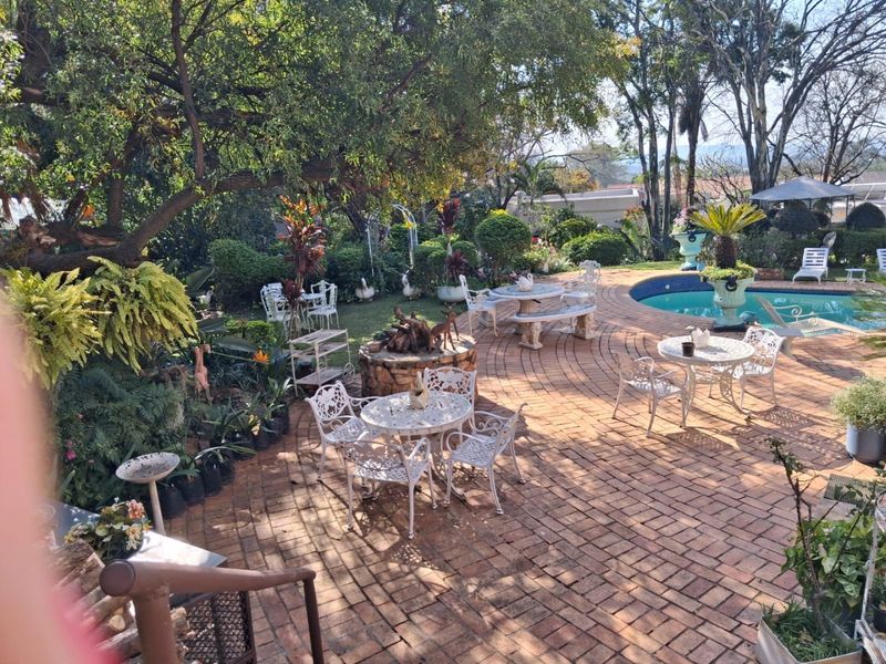 A spacious outdoor entertainment area featuring a swimming pool, extensive brick paving, and a mature landscaped garden setting.