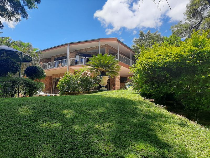A view of the rear elevation of the house, featuring a spacious covered balcony, brick exterior, and a well-maintained landscaped garden.