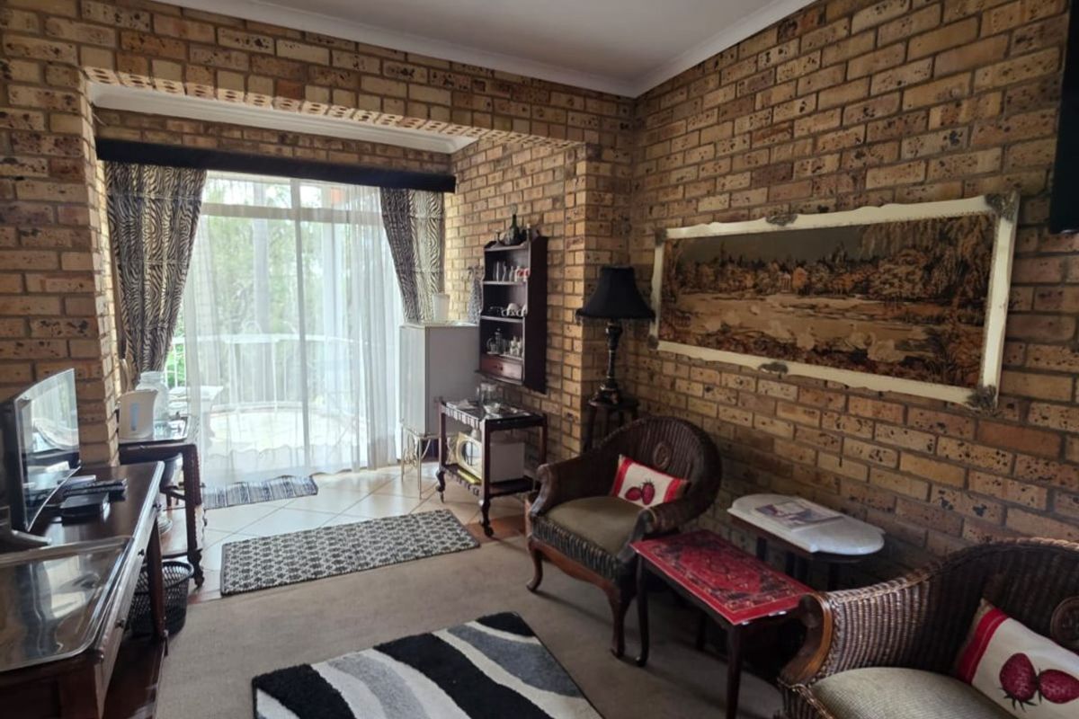 A living room featuring exposed brick walls, carpeted flooring, and a sliding glass door providing access to an outdoor area.