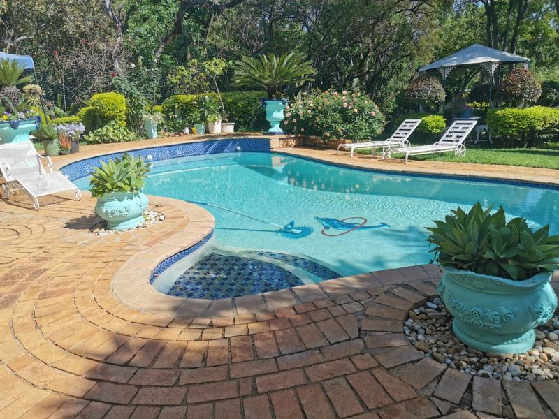 A well-maintained swimming pool area featuring brick paving, mosaic tile detailing, and established garden landscaping.