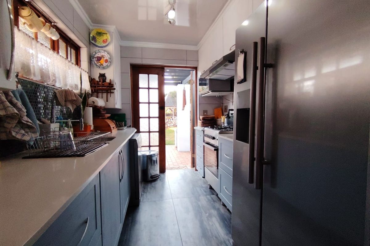 A functional galley-style kitchen featuring modern grey cabinetry, stone countertops, tiled backsplash, and direct access to the rear garden through a glass panel door.