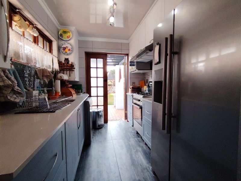 A functional galley-style kitchen featuring modern grey cabinetry, stone countertops, tiled backsplash, and direct access to the rear garden through a glass panel door.