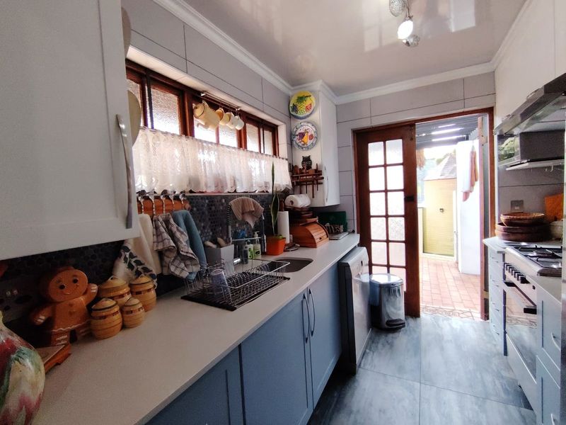 A functional kitchen featuring modern blue cabinetry, a gas hob with extractor, tiled backsplash, and direct access to an outdoor patio area.