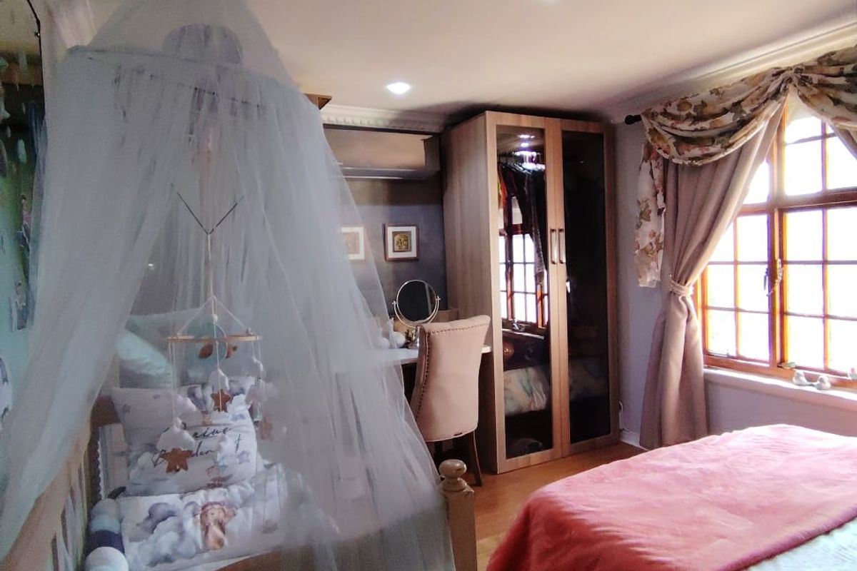 A well-maintained bedroom featuring timber flooring, built-in wardrobe storage, an air conditioning unit, and large timber-framed windows allowing for natural light.