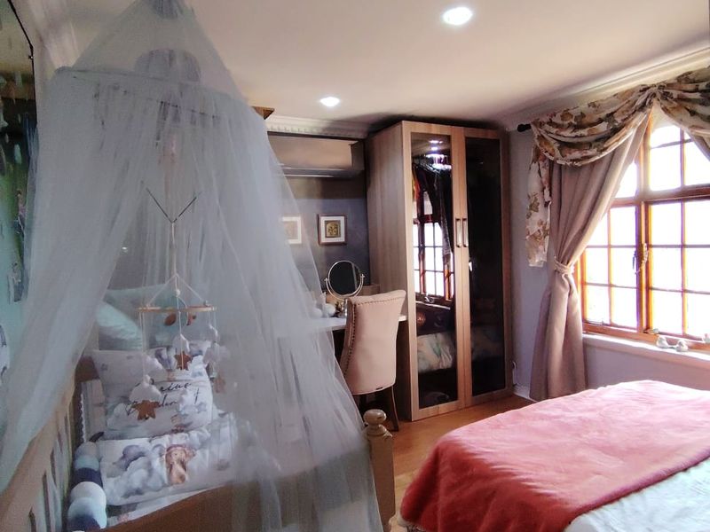 A well-maintained bedroom featuring timber flooring, built-in wardrobe storage, an air conditioning unit, and large timber-framed windows allowing for natural light.