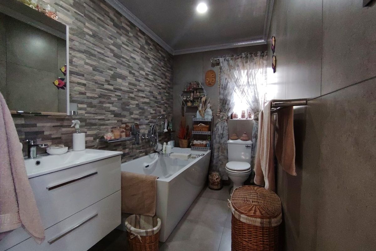 A well-maintained bathroom featuring a modern vanity, bathtub, toilet, and a decorative stone-look tiled feature wall.