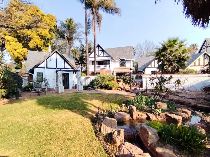 A well-maintained rear garden featuring a stone water feature, paved patio area, and charming Tudor-style architecture with a balcony.
