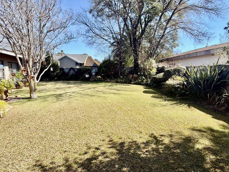 A spacious rear garden featuring a well-maintained lawn, mature trees, and perimeter boundary walls, providing a private outdoor space.