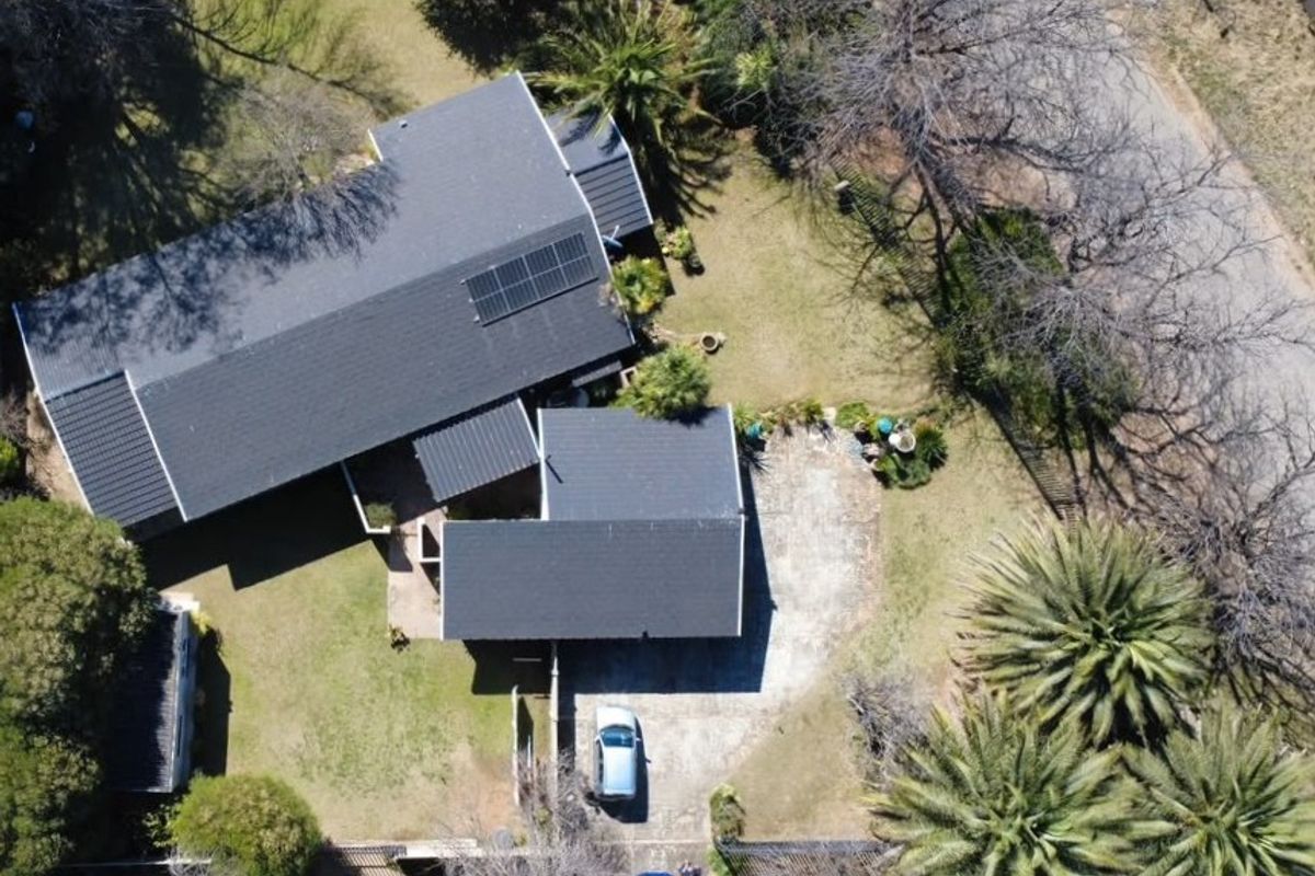 Aerial view of the property showcasing the roof structure, solar panel installation, paved driveway, and surrounding garden area.