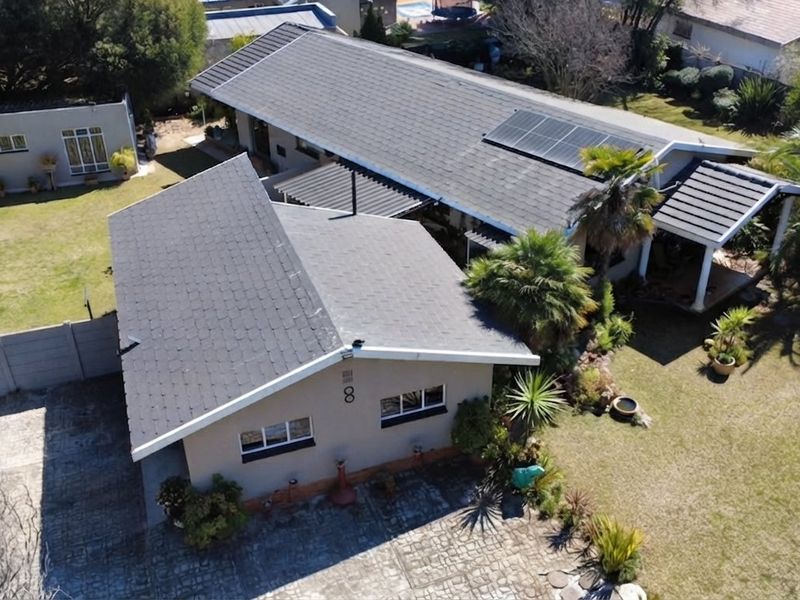 Aerial view of a residential property featuring a tiled roof with solar panels, a paved driveway, and a well-maintained garden with a covered patio area.