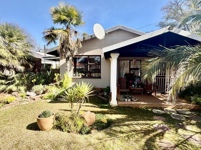 A well-maintained rear exterior view featuring a covered patio with concrete columns, tiled flooring, and a landscaped garden area.