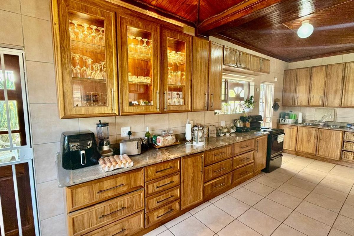 Spacious kitchen featuring extensive wooden cabinetry, granite countertops, tiled flooring, and a distinctive timber ceiling with integrated display lighting.