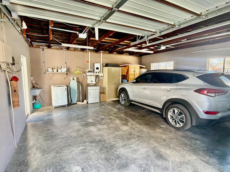 Spacious garage featuring exposed timber roof trusses, concrete flooring, and integrated utility area with a wall-mounted sink and water heater.