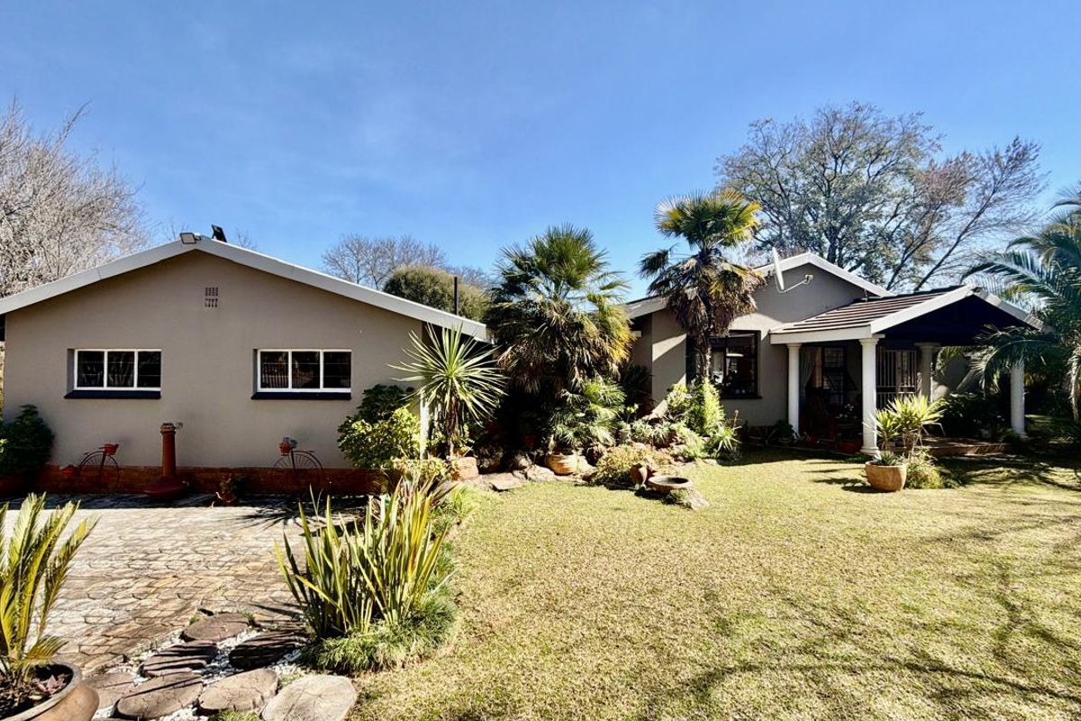A well-maintained rear exterior view featuring a paved driveway, landscaped garden, and a covered patio area with structural columns.
