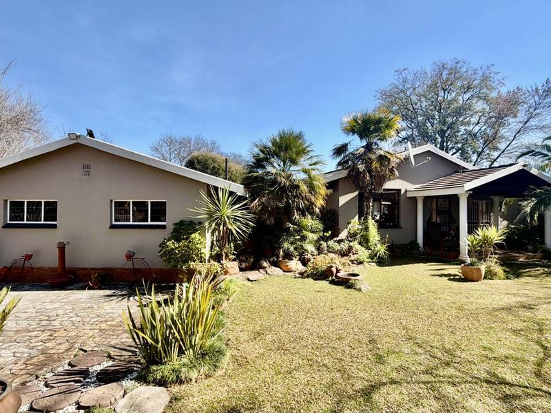 A well-maintained rear exterior view featuring a paved driveway, landscaped garden, and a covered patio area with structural columns.