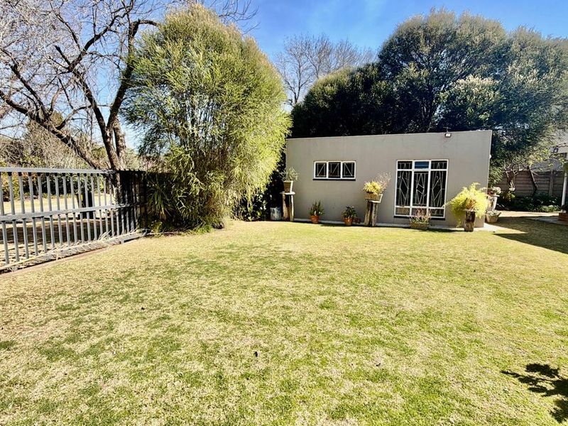 A well-maintained garden area featuring a manicured lawn, mature trees, and a secure metal perimeter fence with a sliding gate.