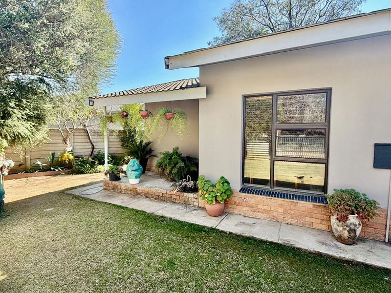 A view of the rear exterior featuring a covered patio area, brick base detailing, and aluminium window frames overlooking a landscaped garden.