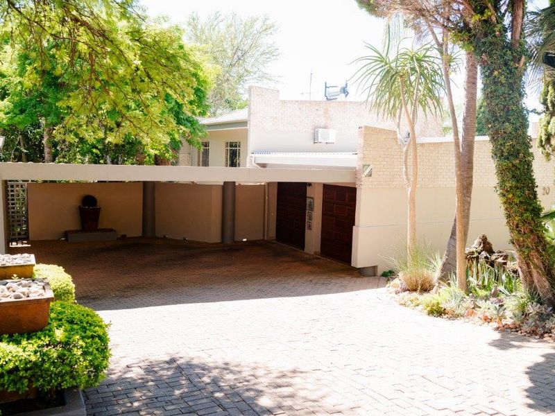 Front view of the property featuring a paved driveway, double garage, and a covered carport area surrounded by established garden landscaping.