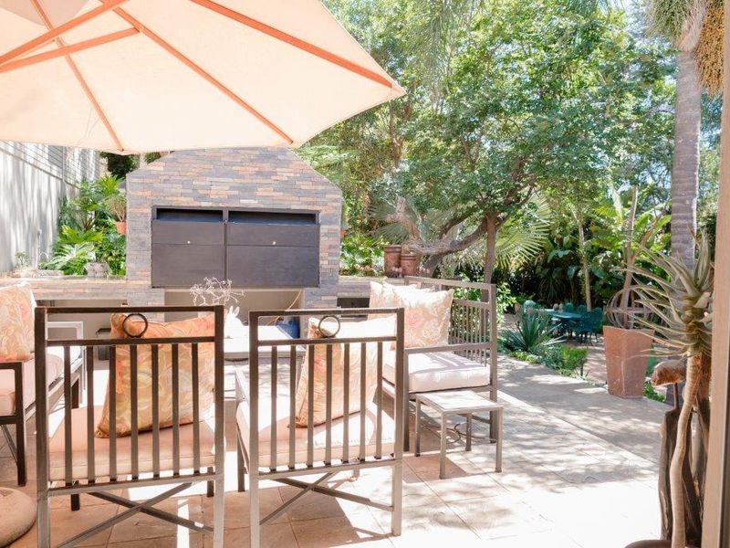 Outdoor patio area featuring a built-in stone-clad braai and tiled flooring, set within a lush, leafy garden environment.