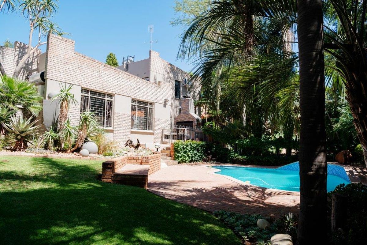 Rear view of the property featuring a swimming pool, paved patio area with a built-in braai, and a well-established garden.