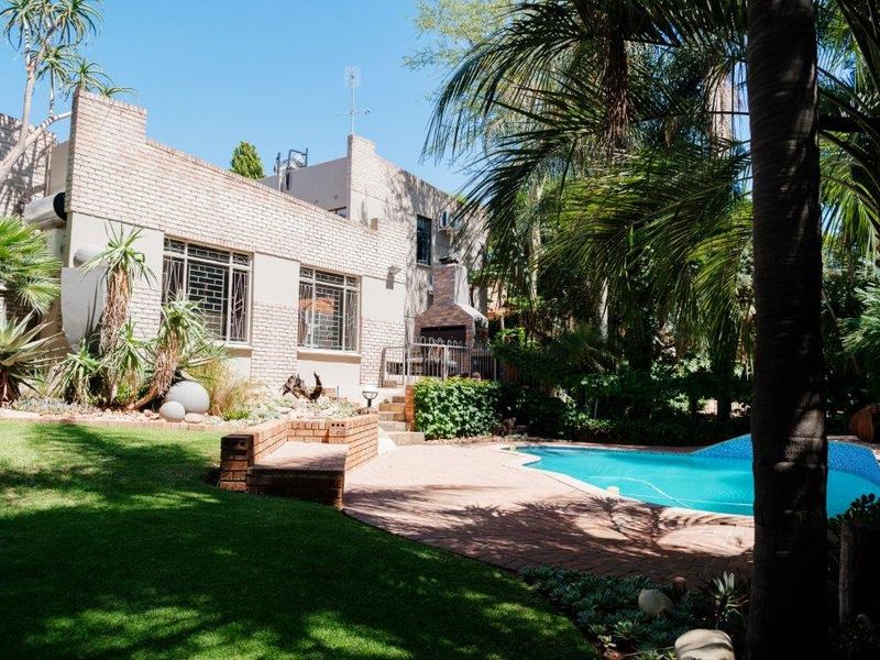 Rear view of the property featuring a swimming pool, paved patio area with a built-in braai, and a well-established garden.
