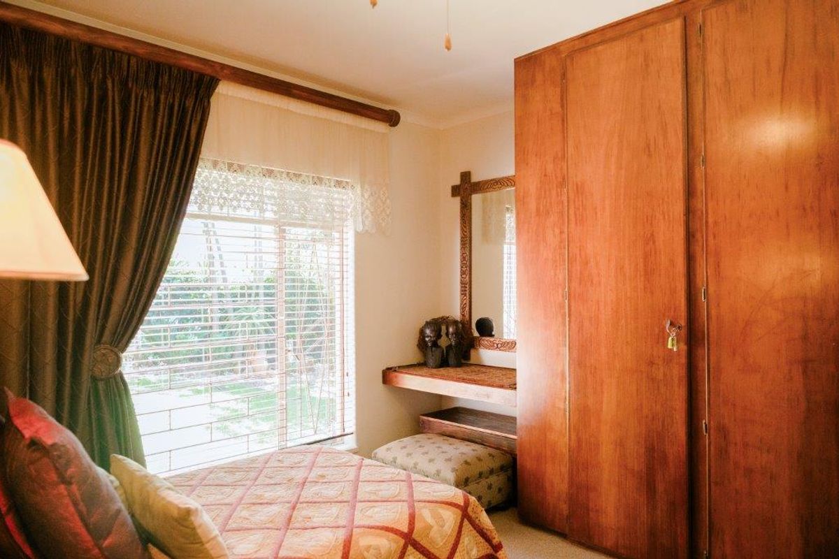A bedroom featuring a large built-in wooden wardrobe, a wall-mounted vanity shelf, and a window with security bars.