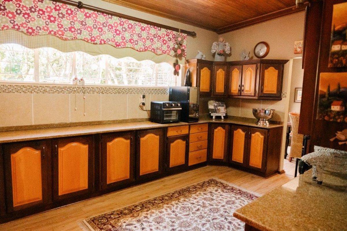 A traditional kitchen featuring two-tone laminate cabinetry, granite countertops, a tiled backsplash, and a warm timber ceiling.