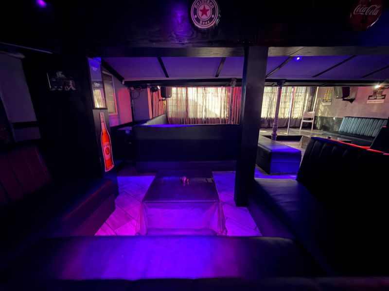 A commercial bar area featuring built-in booth seating, support columns, and tiled flooring, illuminated with purple ambient lighting.