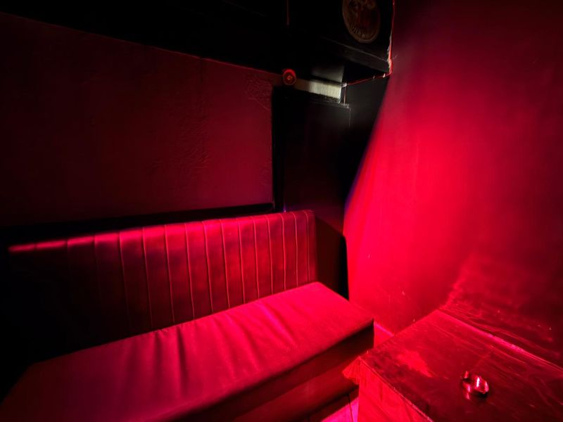 A dimly lit bar area featuring built-in bench seating and dark wall finishes, illuminated by red accent lighting.