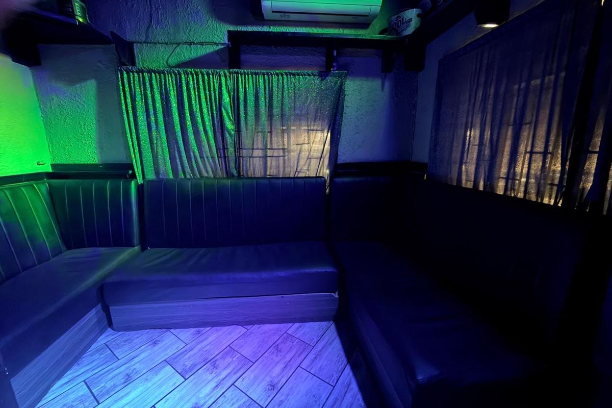 A lounge area featuring built-in bench seating, tiled flooring, and a wall-mounted air conditioning unit, illuminated by ambient colored lighting.