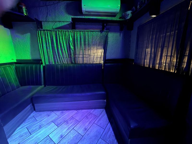 A lounge area featuring built-in bench seating, tiled flooring, and a wall-mounted air conditioning unit, illuminated by ambient colored lighting.