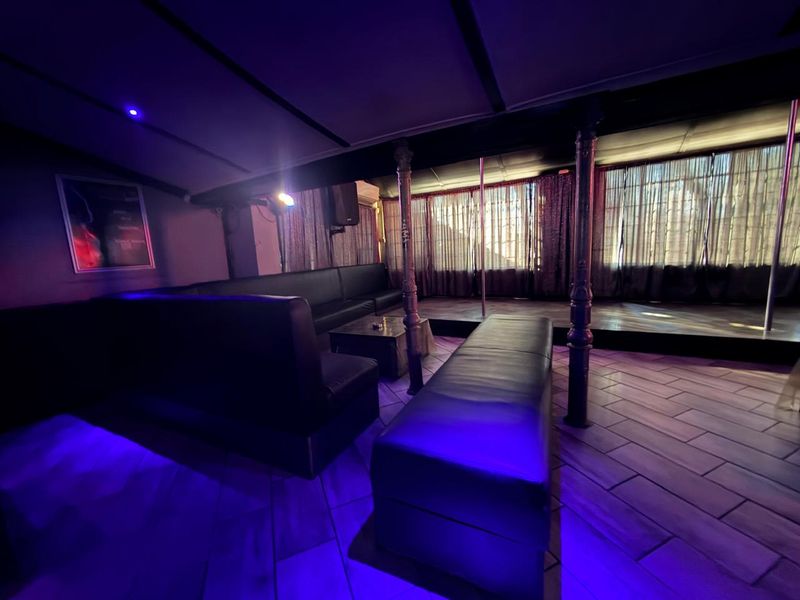 A commercial bar area featuring a raised stage with a dance pole, decorative columns, and integrated accent lighting.