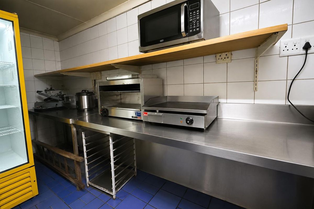 Commercial kitchen prep area featuring stainless steel work surfaces, tiled wall splashbacks, and functional built-in shelving for efficient food preparation.