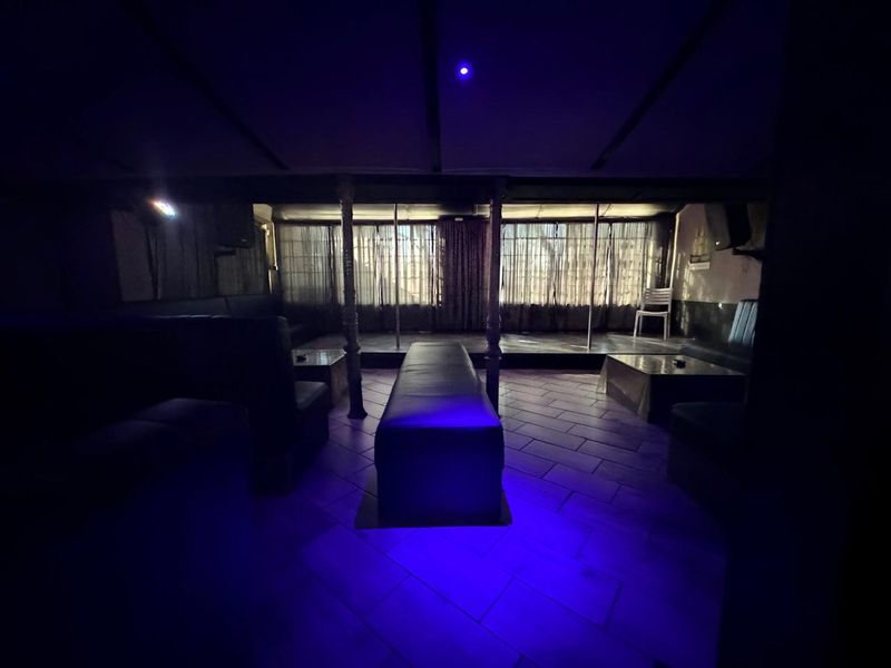 Commercial clubhouse space featuring a raised stage with dance poles, tiled flooring, and integrated support columns in a dimly lit environment.