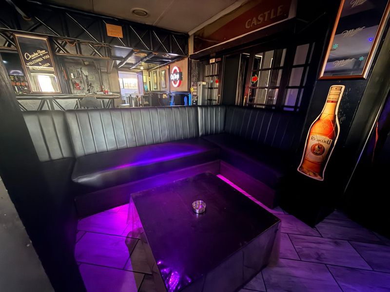 A commercial bar area featuring built-in corner booth seating, tiled flooring, and ambient purple accent lighting, creating a lounge-style atmosphere.
