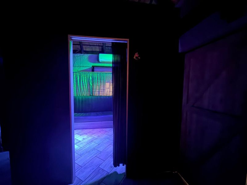 A view through a doorway into a room featuring tiled flooring, a thatch ceiling, and an air conditioning unit, illuminated by colored lighting.