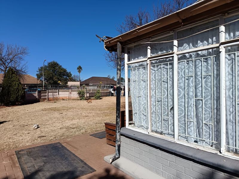Rear exterior view of the property featuring a paved patio area, security-barred windows, and a garden space with boundary walling.