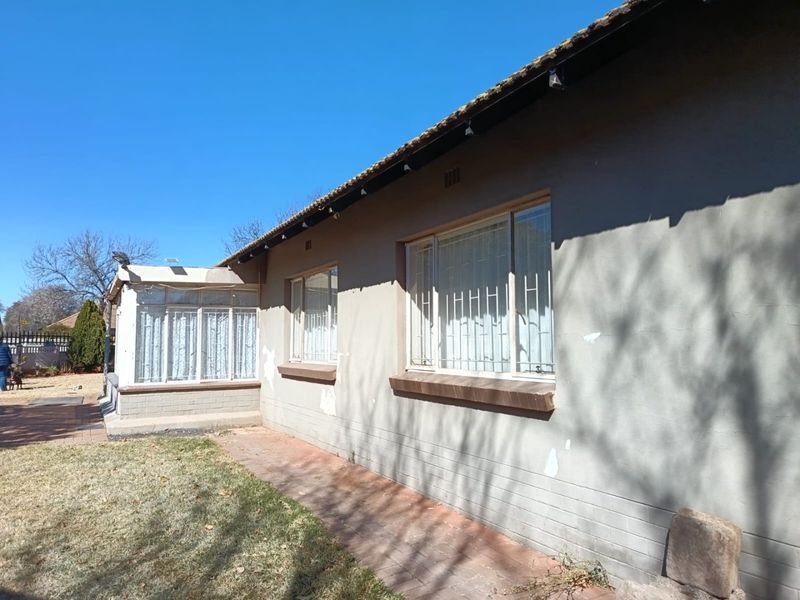 Rear view of the house showing a brick exterior with security bars on windows, a tiled roof, and a paved walkway.