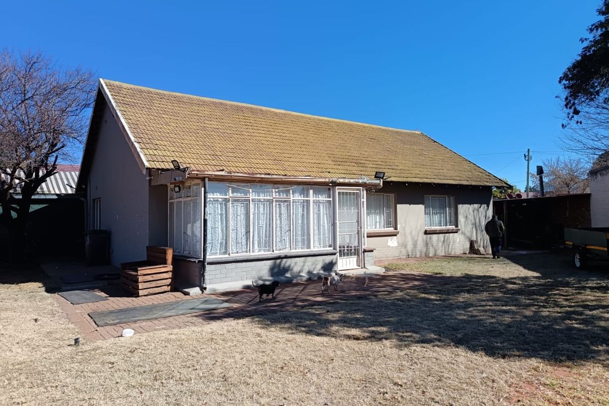 Rear view of the house featuring a tiled roof, an enclosed sunroom, and a paved patio area leading to the garden.